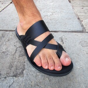 May include: Black leather sandals with a criss-cross strap design. The sandals have a simple, flat sole.
