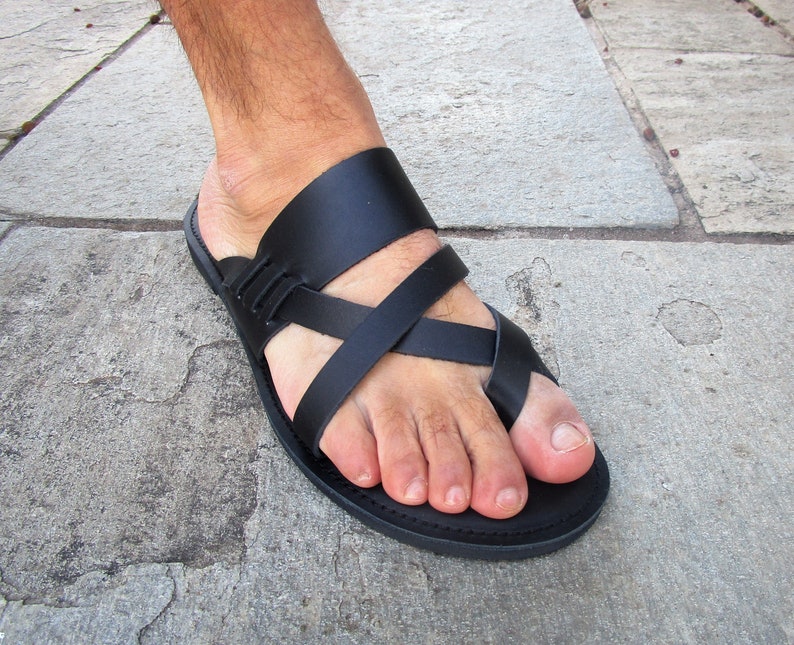 May include: Black leather sandals with a criss-cross strap design. The sandals have a simple, flat sole.