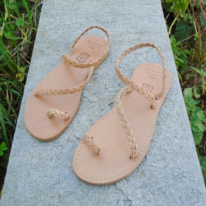 May include: A pair of tan leather sandals with braided straps. The sandals have a toe loop and an ankle strap. The sandals are made by "Andalousite Made with Pride Athens".