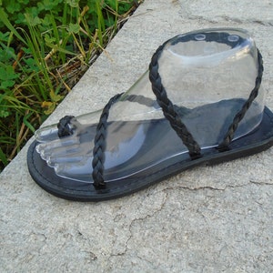 May include: Black leather sandals with braided straps. The sandals have a flat sole and are designed to be worn with bare feet.