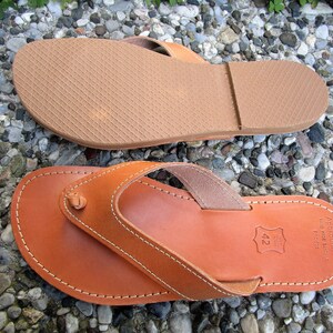 May include: A pair of brown leather sandals with a thong strap and a stitched edge. The sandals have a rubber sole and are labeled "Apropos Shoes" with the size "42" printed on the sole.