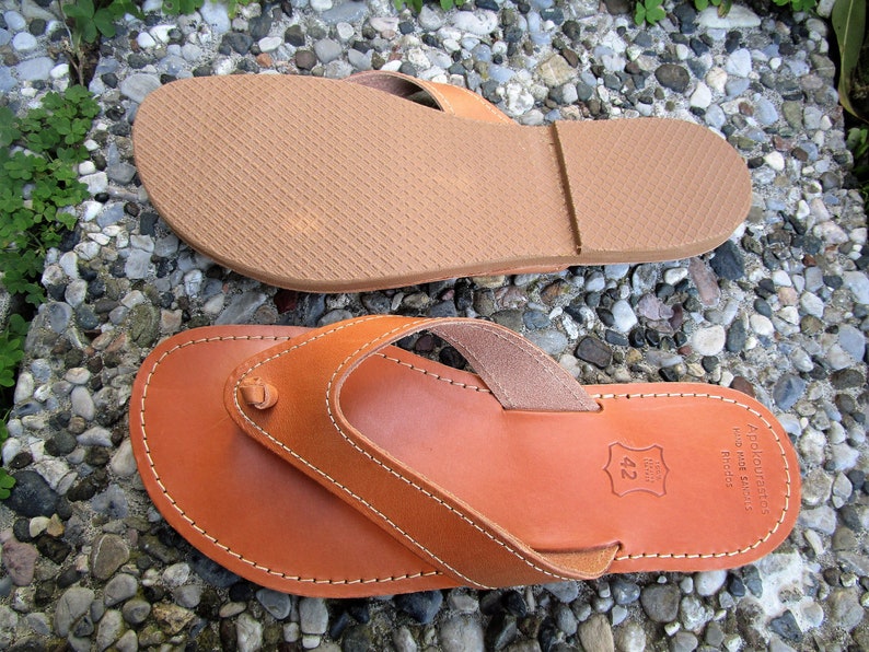 May include: A pair of brown leather sandals with a thong strap and a stitched edge. The sandals have a rubber sole and are labeled "Apropos Shoes" with the size "42" printed on the sole.