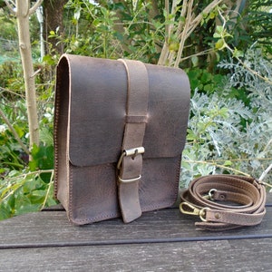 May include: A brown leather crossbody bag with a flap closure and a buckle. The bag has a long adjustable strap and is made of distressed leather.