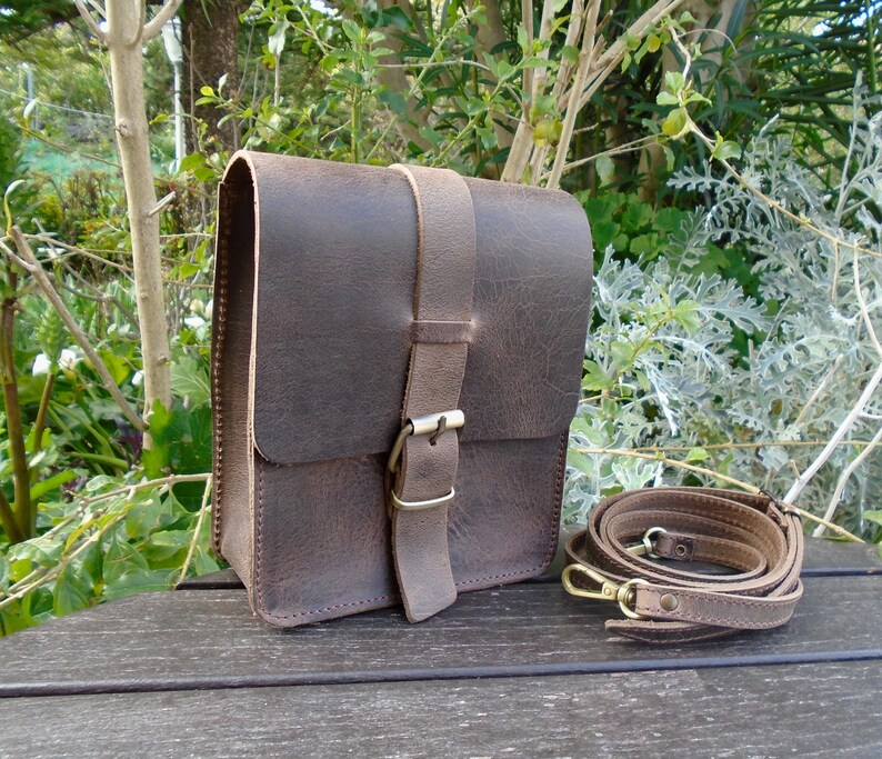 May include: A brown leather crossbody bag with a flap closure and a buckle. The bag has a long adjustable strap and is made of distressed leather.