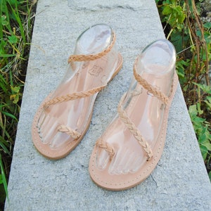 May include: A pair of tan leather sandals with braided straps. The sandals have a simple design and are perfect for summer.