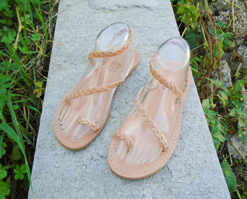 May include: A pair of tan leather sandals with braided straps. The sandals have a simple design and are perfect for summer.