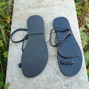 May include: A pair of black leather sandals with braided straps. The sandals have a flat sole and are tied at the ankle.