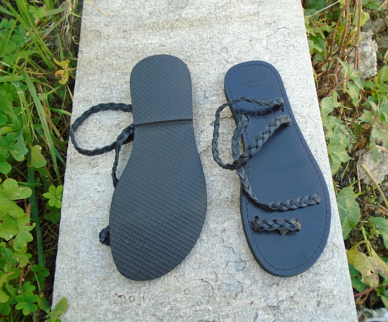 May include: A pair of black leather sandals with braided straps. The sandals have a flat sole and are tied at the ankle.