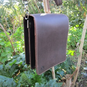 May include: A brown leather messenger bag with a long strap and a silver clasp. The bag has a flap closure and a small pocket on the front.