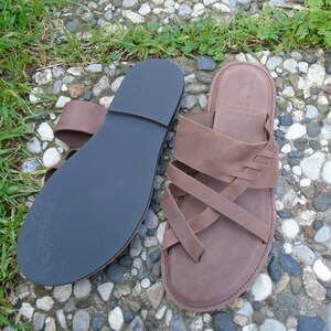 May include: A pair of brown leather sandals with a criss-cross strap design. The sandals have a black rubber sole.
