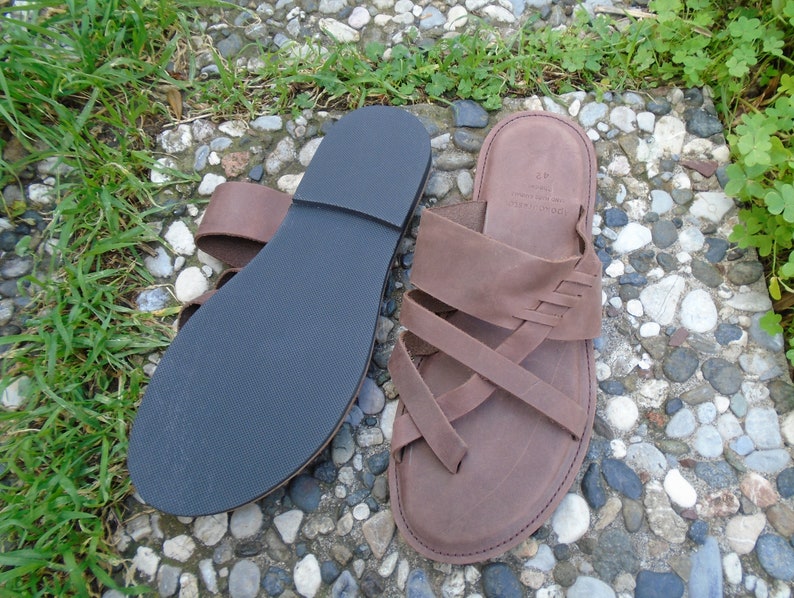 May include: A pair of brown leather sandals with a criss-cross strap design. The sandals have a black rubber sole.