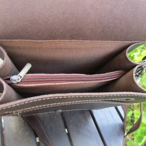 May include: A brown leather bag with a zippered top and a long strap. The bag is open and the inside is visible.
