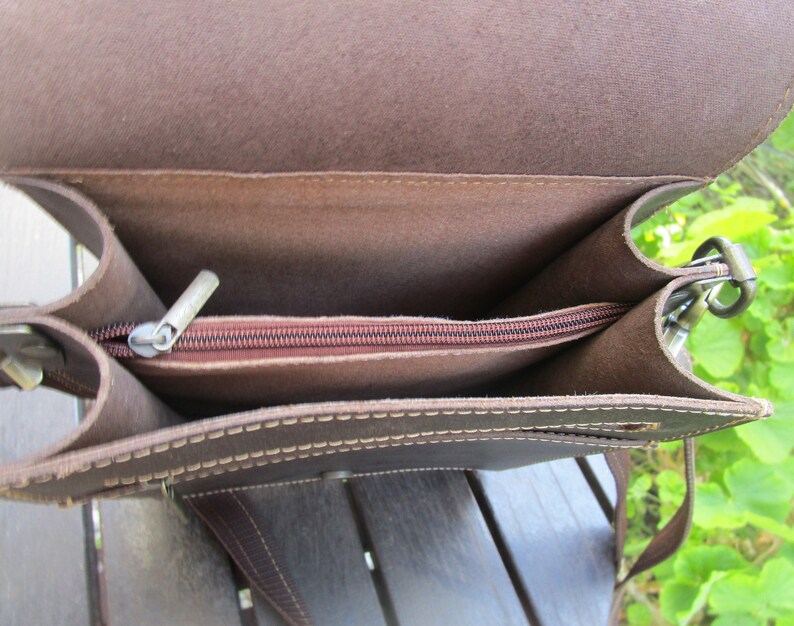 May include: A brown leather bag with a zippered top and a long strap. The bag is open and the inside is visible.