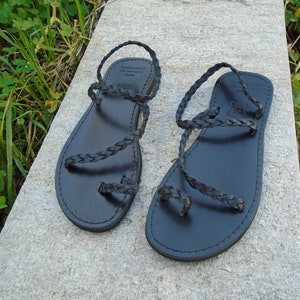 May include: Black leather sandals with braided straps. The sandals have a simple design and are perfect for summer.