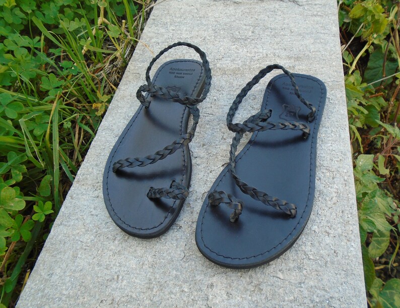 May include: Black leather sandals with braided straps. The sandals have a simple design and are perfect for summer.
