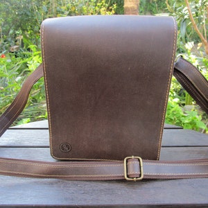 May include: A brown leather messenger bag with a long adjustable strap. The bag has a flap closure and a small logo on the front.
