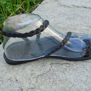 May include: Black leather sandals with braided straps. The sandals have a flat sole and are made of a soft, supple leather.
