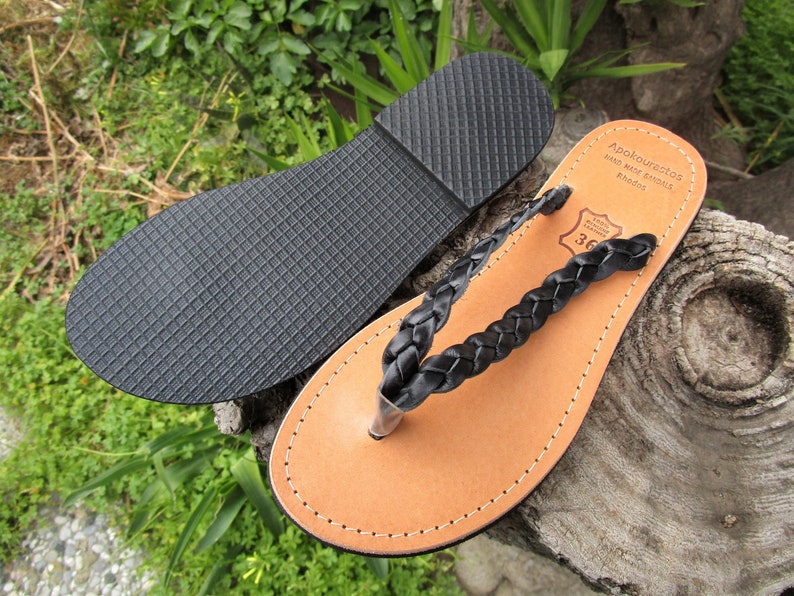 Pu&ograve; includere: Sandali a listino in pelle intrecciata nera con suola in pelle marrone. I sandali hanno una suola in gomma ed sono etichettati "Apokoronastos Hand Made Sandals Rhodes 36".