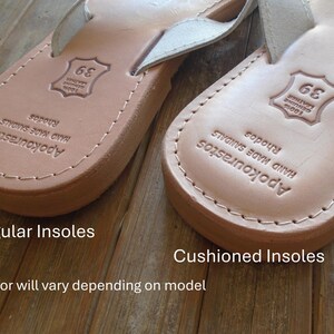 Pu&ograve; includere: Primo piano di due sandali in pelle con suole interne diverse. Il sandalo a sinistra ha una suola interna normale, mentre il sandalo a destra ha una suola interna imbottita. Entrambe le sandali hanno il testo "Apokourastos HAND MADE SANDALS Rhodos" e un'etichetta di taglia.