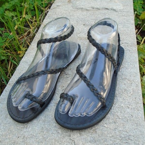 May include: A pair of black leather sandals with braided straps. The sandals have a simple design and are perfect for summer.