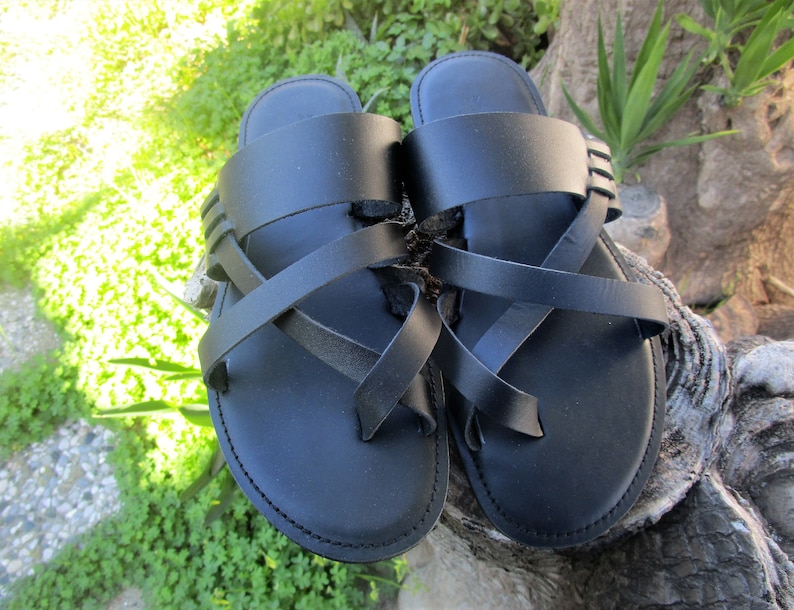 May include: A pair of black leather sandals with criss-cross straps. The sandals have a simple design and are perfect for warm weather.
