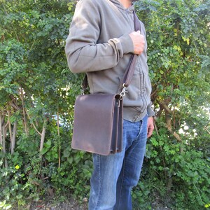 May include: A brown leather messenger bag with a long adjustable strap. The bag has a flap closure and a silver buckle.