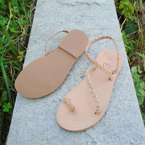May include: A pair of light brown leather sandals with braided straps. The sandals have a simple design and are made of high-quality leather.