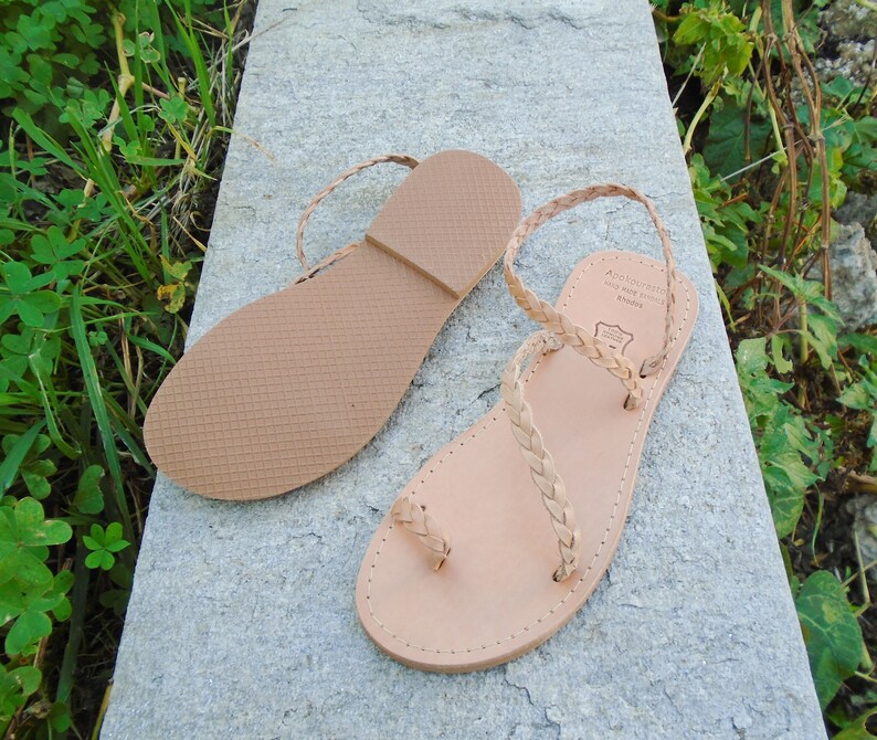 May include: A pair of light brown leather sandals with braided straps. The sandals have a simple design and are made of high-quality leather.