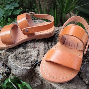 K&ouml;nnte beinhalten: Ein Paar braune Ledersandalen mit zwei Riemen und einem Schnallenverschluss. Die Sandalen sind Gr&ouml;&szlig;e 22.
