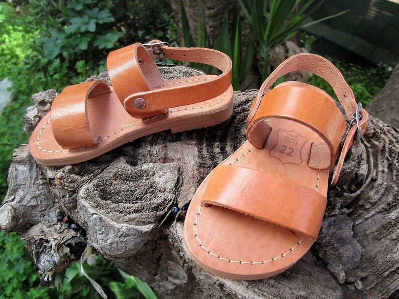K&ouml;nnte beinhalten: Ein Paar braune Ledersandalen mit zwei Riemen und einem Schnallenverschluss. Die Sandalen sind Gr&ouml;&szlig;e 22.