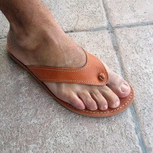 May include: A pair of brown leather thong sandals with a stitched design. The sandals have a simple, minimalist style.