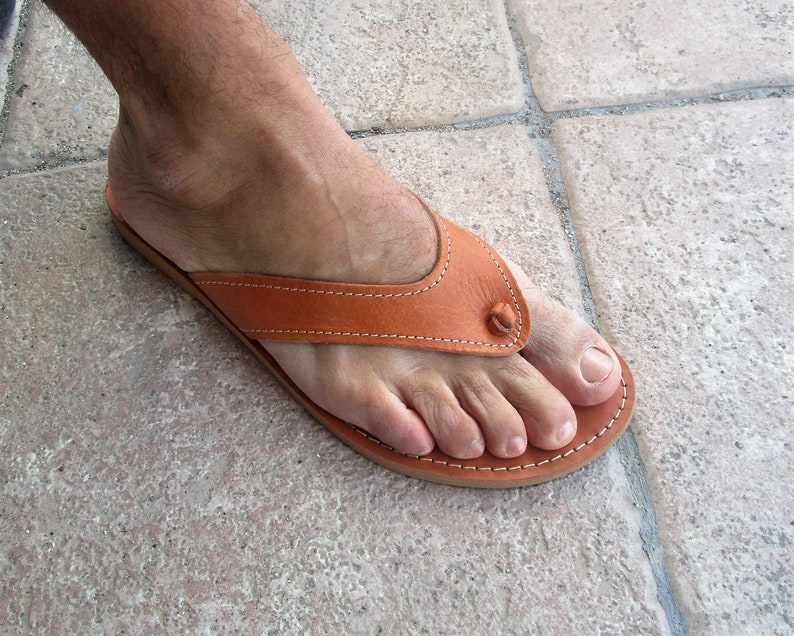 May include: A pair of brown leather thong sandals with a stitched design. The sandals have a simple, minimalist style.