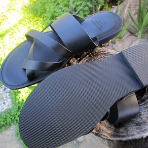 May include: Black leather sandals with a criss-cross strap design. The sandals have a textured rubber sole.