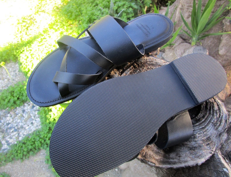 May include: Black leather sandals with a criss-cross strap design. The sandals have a textured rubber sole.