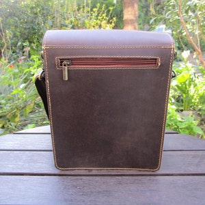 May include: A brown leather messenger bag with a zippered pocket on the back. The bag has a flap closure and a strap.