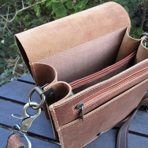 May include: A brown leather messenger bag with a zippered pocket and a flap closure. The bag has a long adjustable strap and a metal clasp.
