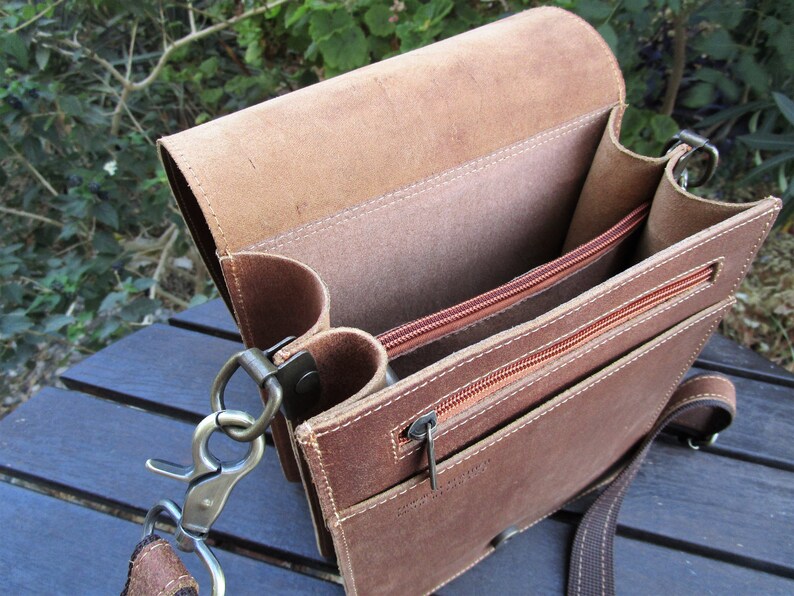 May include: A brown leather messenger bag with a zippered pocket and a flap closure. The bag has a long adjustable strap and a metal clasp.