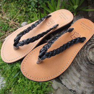 Pu&ograve; includere: Due paia di sandali in pelle nera con cinturini intrecciati. I sandali sono realizzati a Rodi, in Grecia. I sandali sono taglia 36.