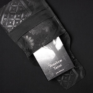 May include: A black fabric pouch with a floral pattern and a black book inside. The book has the title "Tenebræ Tarot" and the author "John Mahoney" printed on the cover.