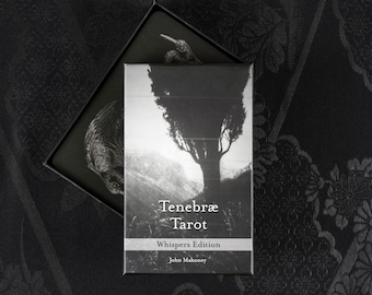 May include: A black and white Tenebræ Tarot deck with a Whispers Edition label. The box features a tree illustration and the name "Tenebræ Tarot". The deck is in a black box with a decorative lid.