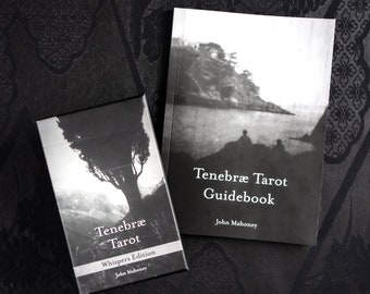 May include: A black and white Tenebræ Tarot deck and guidebook. The deck box features a tree silhouette, while the guidebook displays a landscape image. Both items have the text "Tenebræ Tarot" and "John Mahoney". The deck is the "Whispers Edition".