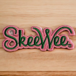 May include: Pink and green embroidered patch with the word "SkeewEe" in a cursive font.