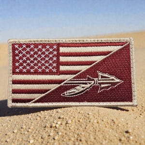 May include: Embroidered patch featuring a split design. One half displays the American flag with red and white stripes and white stars. The other half has a maroon background with a stylized spear and feather design. The patch has a tan border.