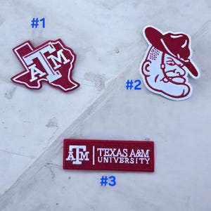 May include: Three embroidered patches featuring Texas A&M University branding. Patch #1 is a maroon Texas-shaped outline with white ATM lettering. Patch #2 is a maroon and white mascot head. Patch #3 is a rectangular maroon bar with white text.