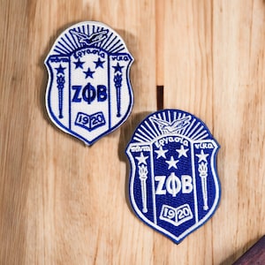 May include: Two blue and white embroidered patches with the letters "ZΦB" and the year "1920" in white. The patches are shaped like shields with a white eagle and three stars at the top.