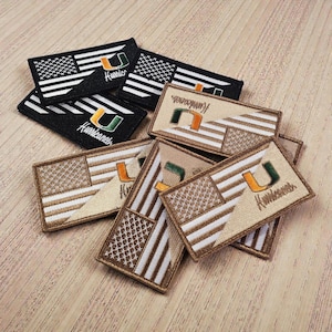May include: Embroidered patches featuring the American flag design with the University of Miami Hurricanes logo. The patches are in black, white, and tan colours. The word "Hurricanes" is embroidered on each patch.