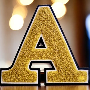 May include: A large, gold felt letter A with black outlining. The letter is raised and has a fuzzy texture.