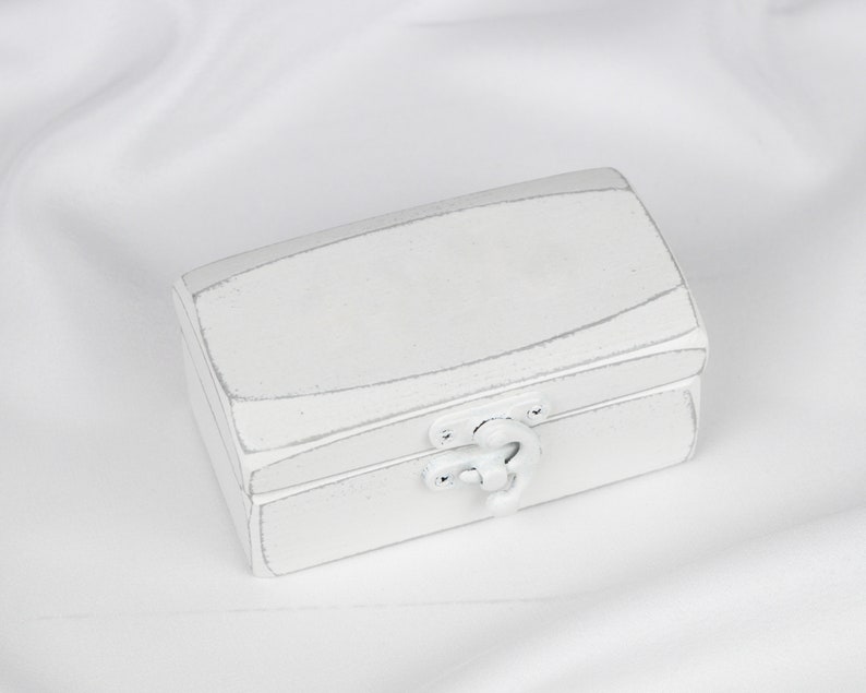 May include: A white wooden box with a hinged lid and a silver latch. The box has a distressed finish, giving it a vintage look.