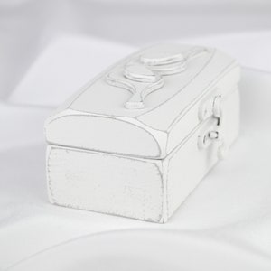 May include: A white wooden box with a carved leaf design on the lid. The box has a hinged lid and a metal latch.
