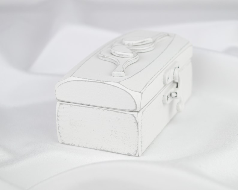 May include: A white wooden box with a carved leaf design on the lid. The box has a hinged lid and a metal latch.